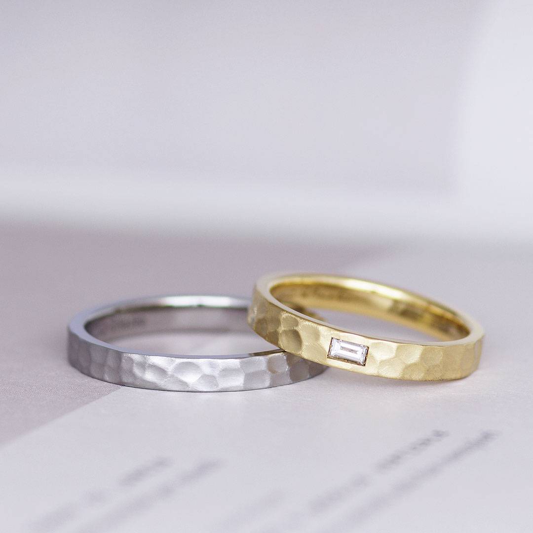 エメラルドカットの宝石を留めた鎚目の結婚指輪（マリッジリング）