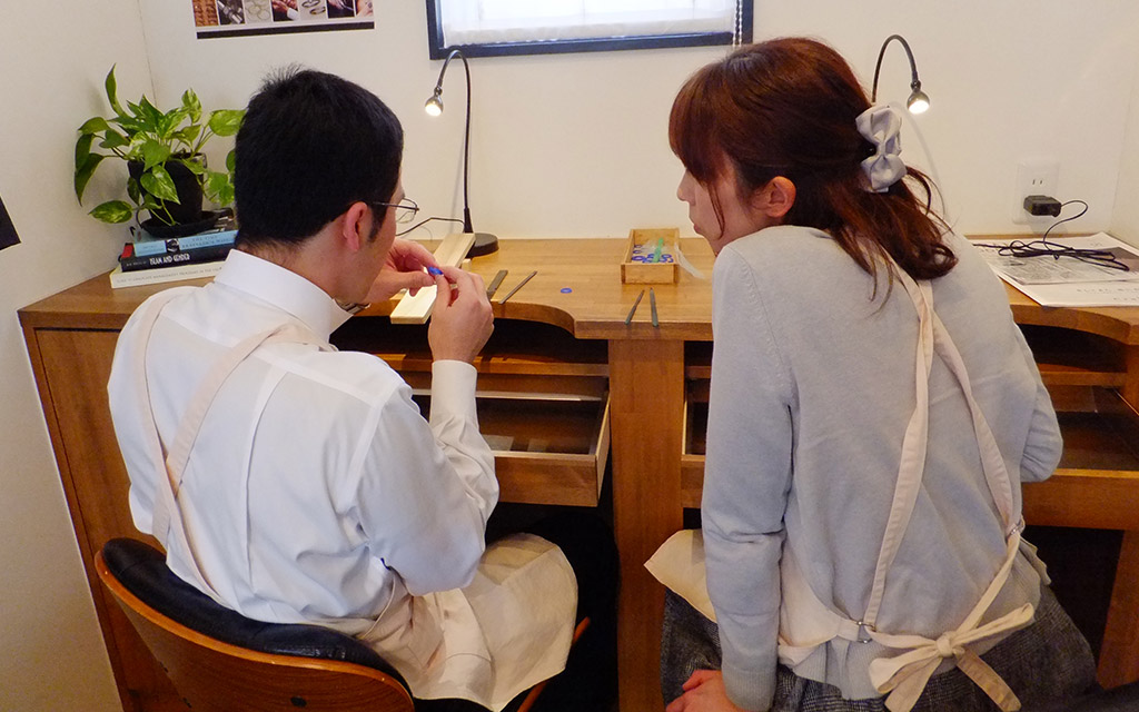 アトリエクラム新潟店で婚約指輪の手作りをしている男性と作業を見守るサプライズプロポーズをうけた女性