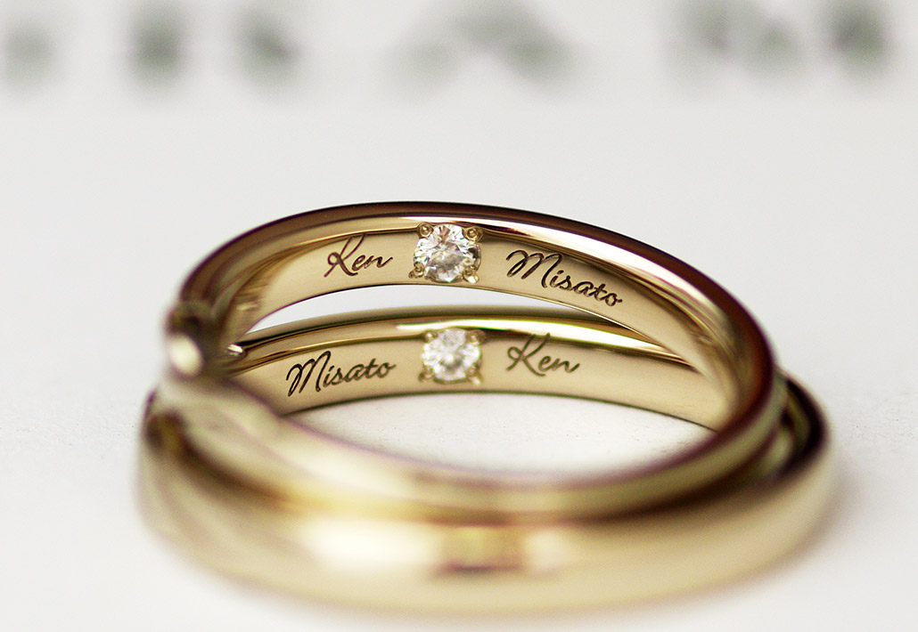 名前の刻印の間にツインダイヤモンドがセッティングされた結婚指輪（マリッジリング）