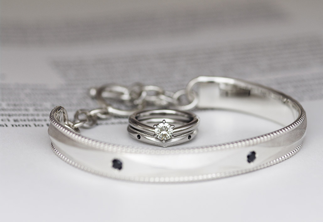 プラチナの婚約指輪とブラックダイヤモンドが留まったV字の結婚指輪とシルバーのバングル