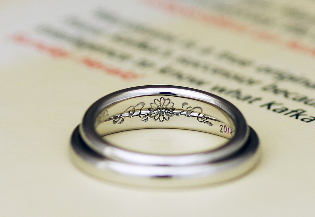 ひまわりとイニシャルを組み合わせたオリジナルデザインが刻印されたプラチナ製の結婚指輪（マリッジリング）の内側